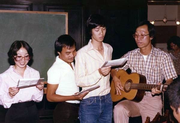 4 people playing a guitar and singing.